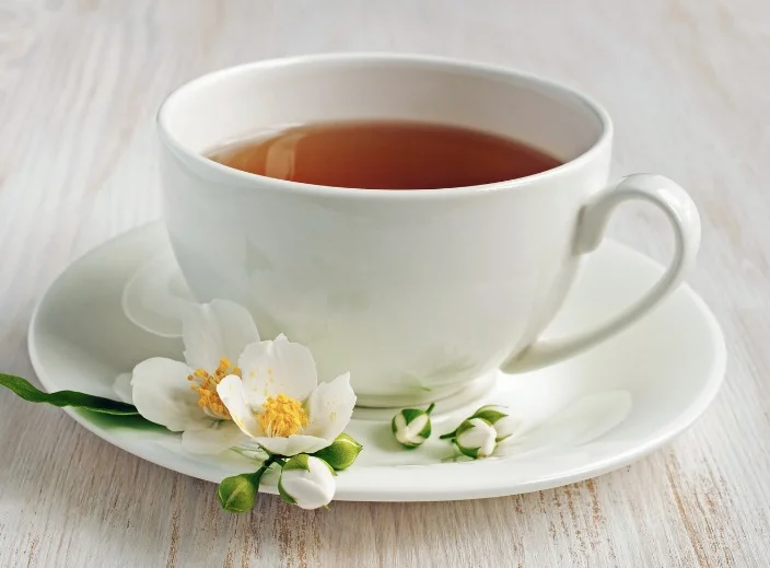 בתמונה: תה יסמין מונח על גבי צלוחית עם פרח יסמין לקישוט בתמונה: תה יסמין מונח על גבי צלוחית עם פרח יסמין לקישוט