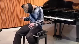אמיתי או טריק? אדם מנגן עם הגב לפסנתר ועיניים עצומות - בעזרת חוטים